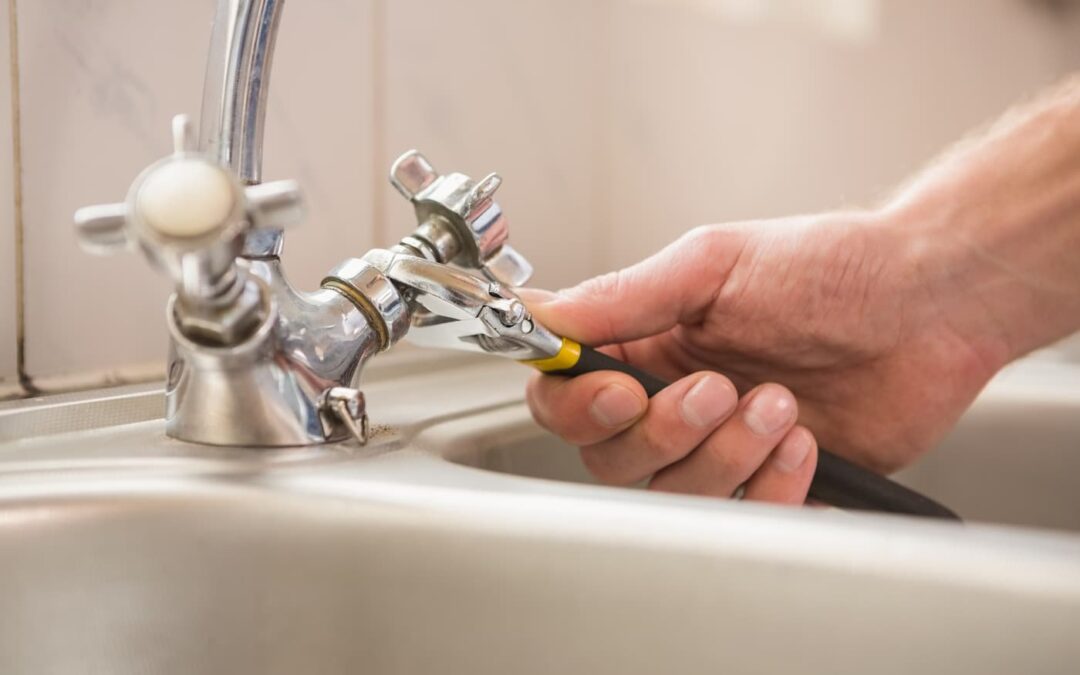 someone using a wrench to tighten a handle on a kitchen sink faucet fufilling tenant maintenance requests