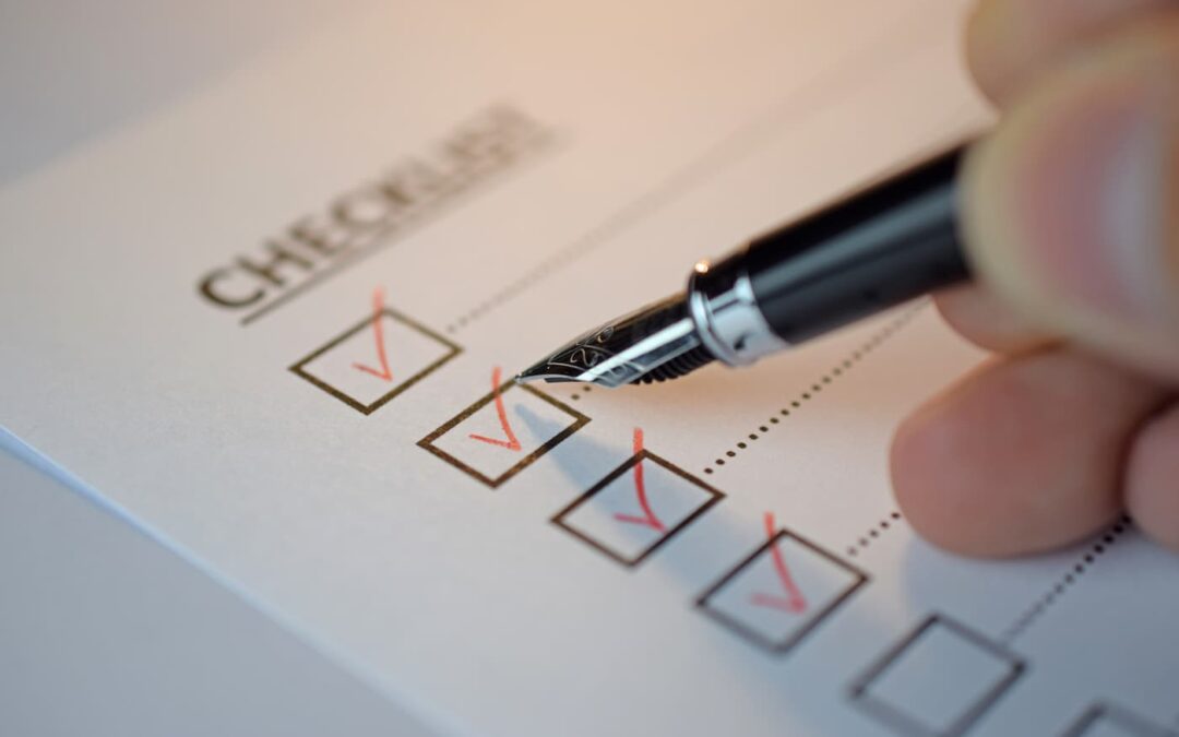 An image of a hand holding a black fountain pen placing red checkmarks on a move-in checklist