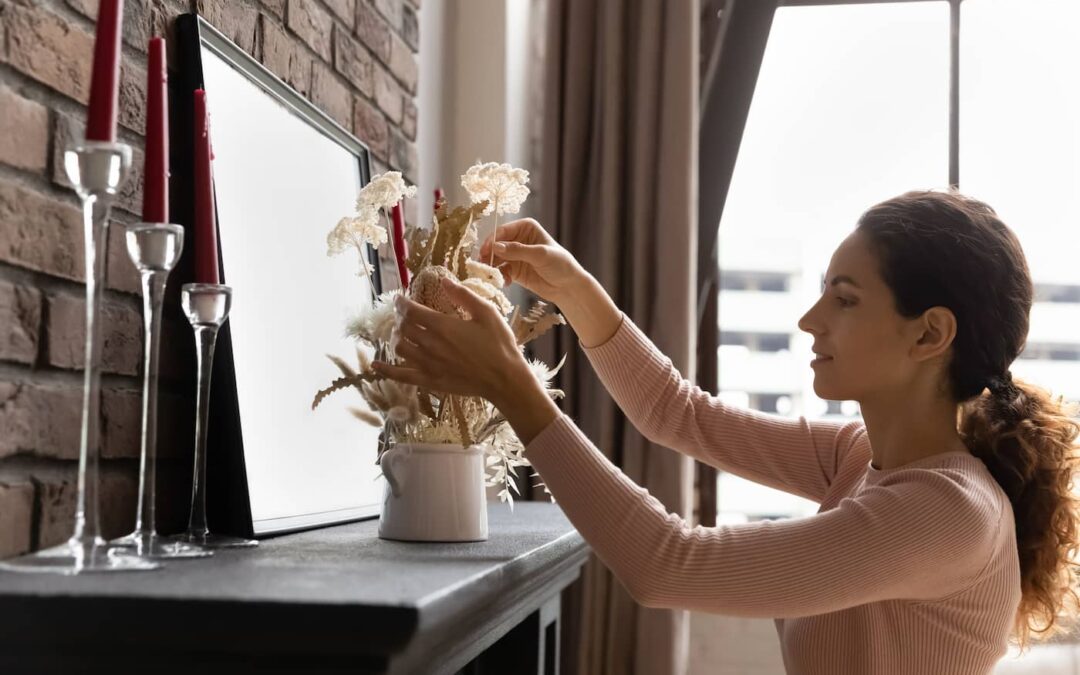 a woman personalizing her rental space by arranging fresh-cut flowers on a fireplace mantel.