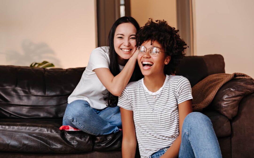 two female roommates sitting together on a couch.