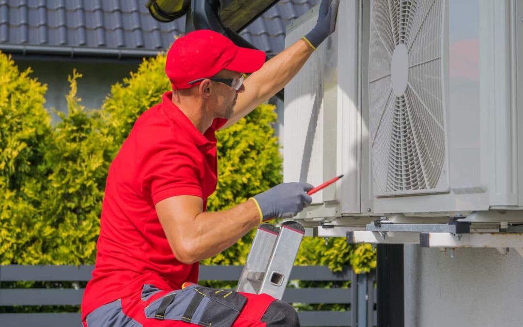 A man wearing a red shirt and hat performs HVAC maintenance on a residential home